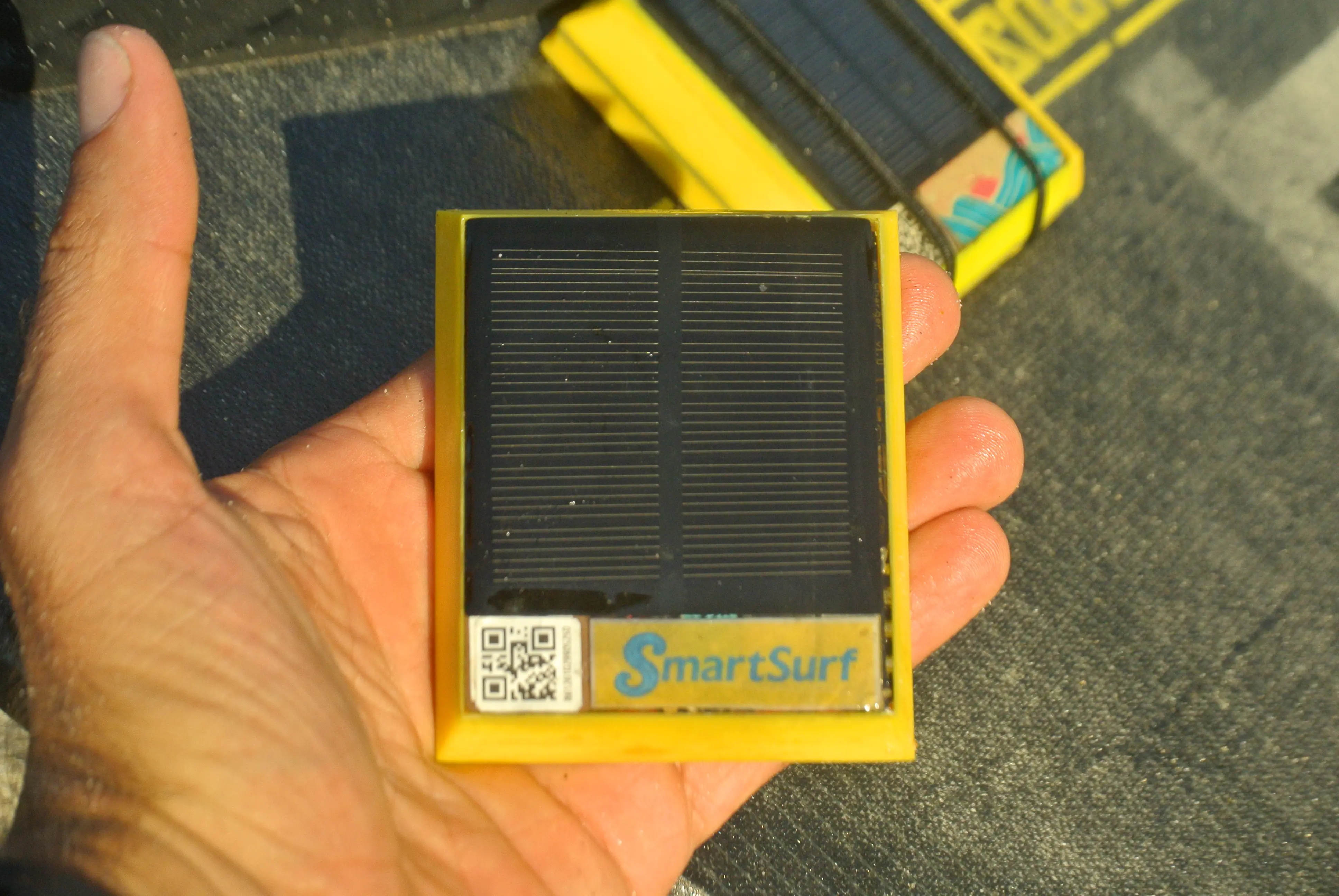 SmartSurf GPS tracker held in hand showing solar panel and SmartSurf branding